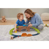 A boy and woman interact with a train track playset featuring a bridge and cargo elements.
