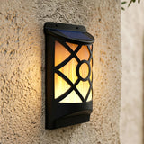 Black solar lantern mounted on a wall, glowing with warm light through geometric cutouts.