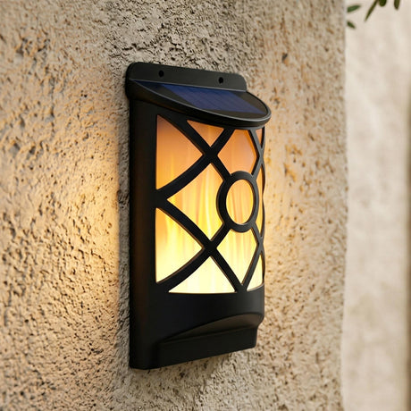 Black solar lantern mounted on a wall, glowing with warm light through geometric cutouts.