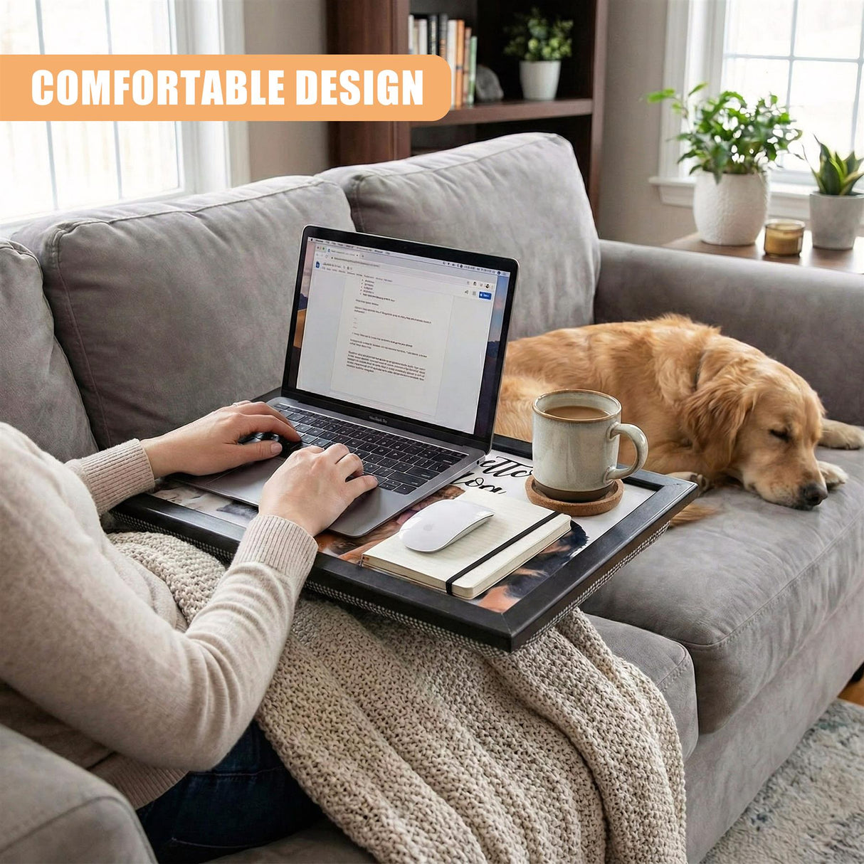 A person sits on a couch, typing on a laptop, with a tray in front of them. The tray holds a laptop, a cup of coffee, a book, and a dog lies nearby. - UKBuyZone