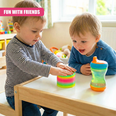 A child plays with a colorful, spiral-shaped toy on a table. The child's friend, also a child, sits nearby, holding a sippy cup. The room is filled with toys and toys are visible in the background. - UKBuyZone