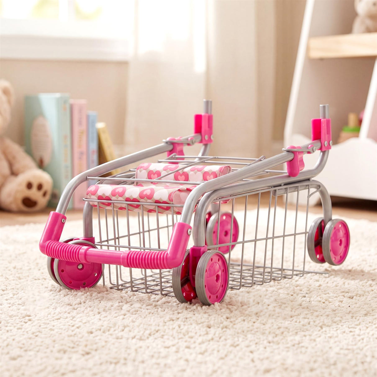 Pink metal toy shopping trolley with a doll seat rests on a cream carpet.