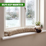 A stuffed dog draught excluder rests on a windowsill alongside small potted plants.