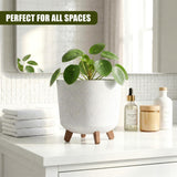 Potted green plant in a light gray, three-legged container rests on a white counter with folded white towels.