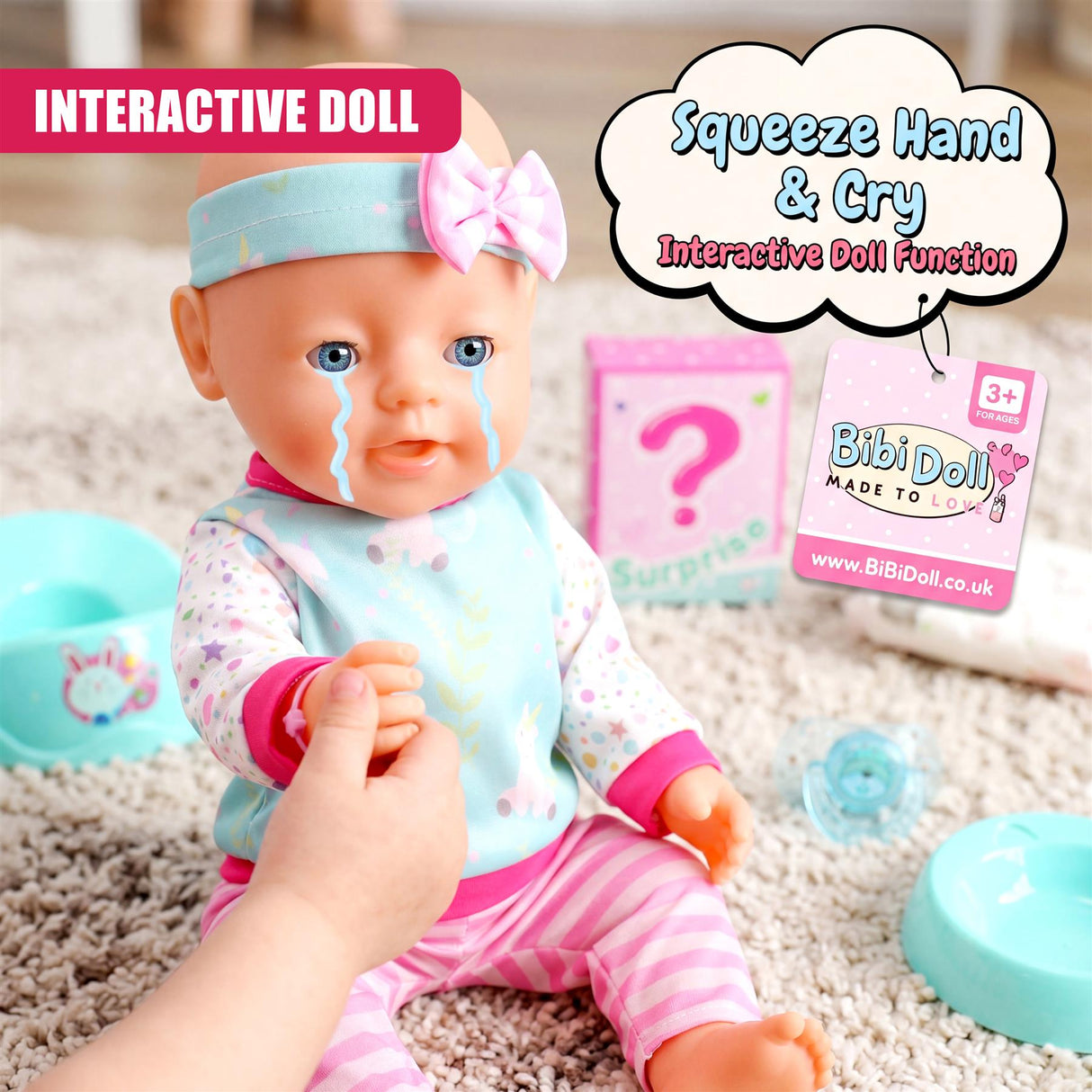 A doll with crying tears is held in hands near small colored tubs and a beige surface.