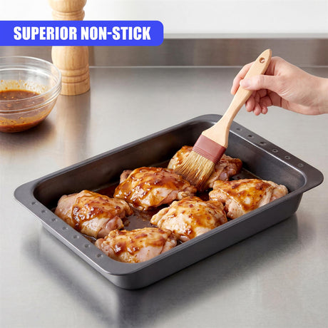 A baking pan holds roasted chicken pieces being brushed with a wooden basting brush.