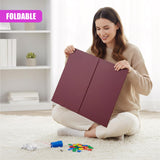 Woman holds a folded ludo board and several colored game pieces on a white rug.