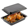 A black roasting tin set holding a roasted chicken and vegetables, covered by a lid.