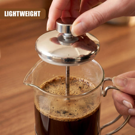 Metal plunger is pressed into a clear glass carafe containing dark roasted coffee.