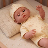 Doll wearing a patterned yellow sleeper and bonnet rests on a cream knitted pillow.
