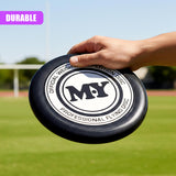 A hand holds a black official flying disc with white lettering and a circular logo.