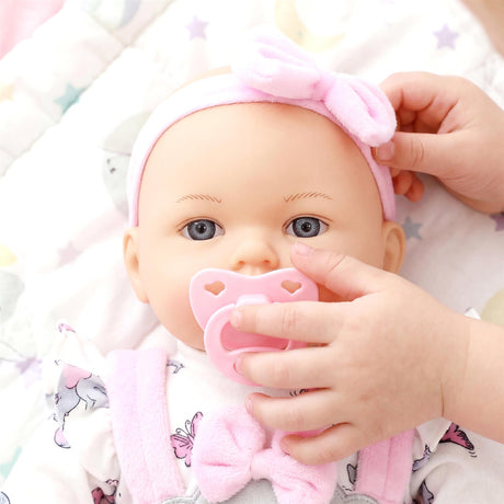 Lifelike baby doll with blue eyes and pink accessories holds a pacifier while resting.