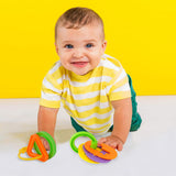 Brightly colored teething toys, grips, and rings are arranged on a surface for infants to explore.