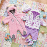 A doll set includes pink and purple hooded outfits and small accessories on a patterned quilted blanket.