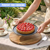 A finished cake on a plate rests on a wooden board with a serving spatula nearby.