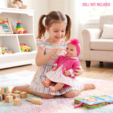 Girl holding a doll in a pink outfit, surrounded by wooden blocks, toys, and living room furniture.