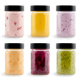 Six small glass jars with black lids holding various colored powdered seasonings.