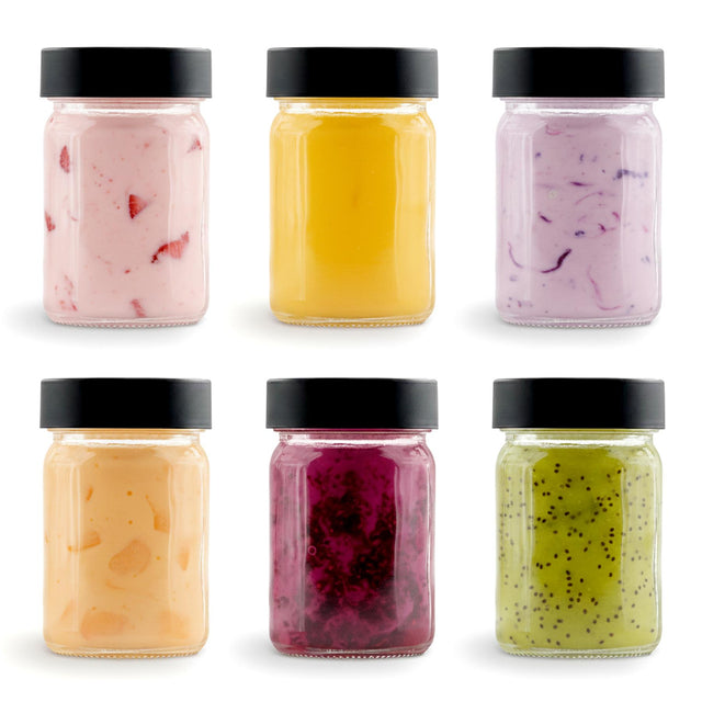 Six small glass jars with black lids holding various colored powdered seasonings.
