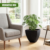 Large, ribbed black planter holding a Monstera plant near a light gray upholstered armchair.
