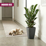 Tall gray flower pot containing a lush green houseplant is displayed on a patterned floor.