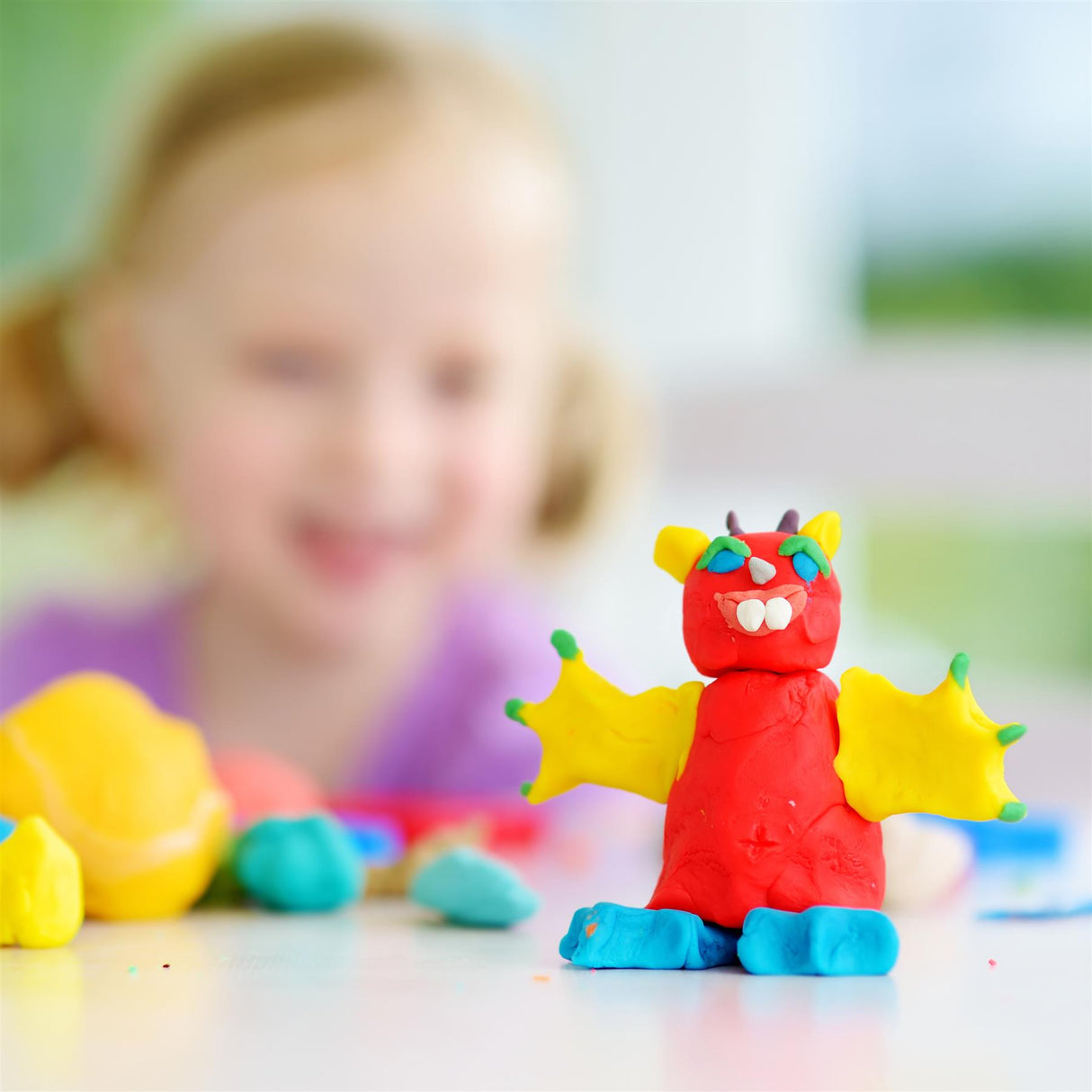 A large red dinosaur made from play dough sitting on a table.