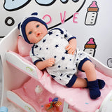 A doll resting in a nursery bed, donned in a blue and white outfit. The doll is seated upright, with the crib being positioned against a pink background adorned with a playful cat motif. - UKBuyZone