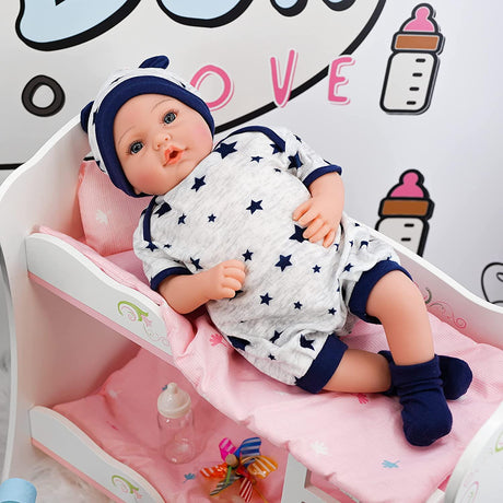 A doll resting in a nursery bed, donned in a blue and white outfit. The doll is seated upright, with the crib being positioned against a pink background adorned with a playful cat motif. - UKBuyZone