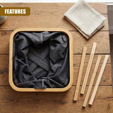 Dark gray fabric inside a square hamper rests on wood near wooden sticks and a folded beige towel.