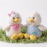 Two white plush chicks and yellow decorative eggs rest in a bed of straw.