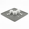 White dishes and metal spoons are displayed on a dark gray rectangular drying mat.