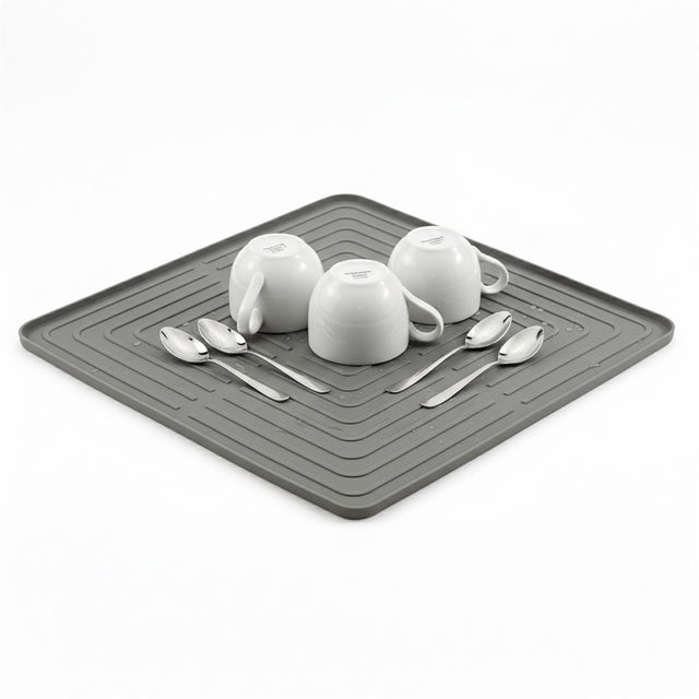 White dishes and metal spoons are displayed on a dark gray rectangular drying mat.