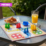 A Ludo board game, colored pieces, dice, pastries, and a drink sit on an outdoor table.