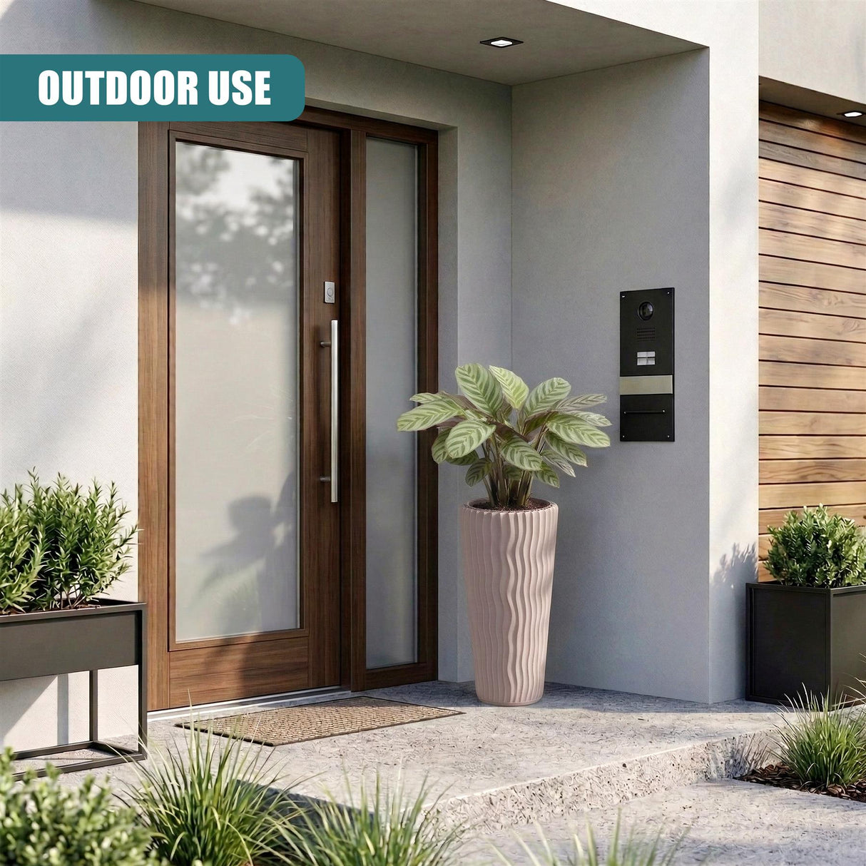 Ribbed, light brown outdoor pot holding a plant, positioned next to a modern entryway door.