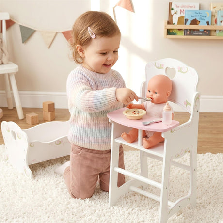 Girl feeding a doll at a white wooden high chair structure next to a doll crib.