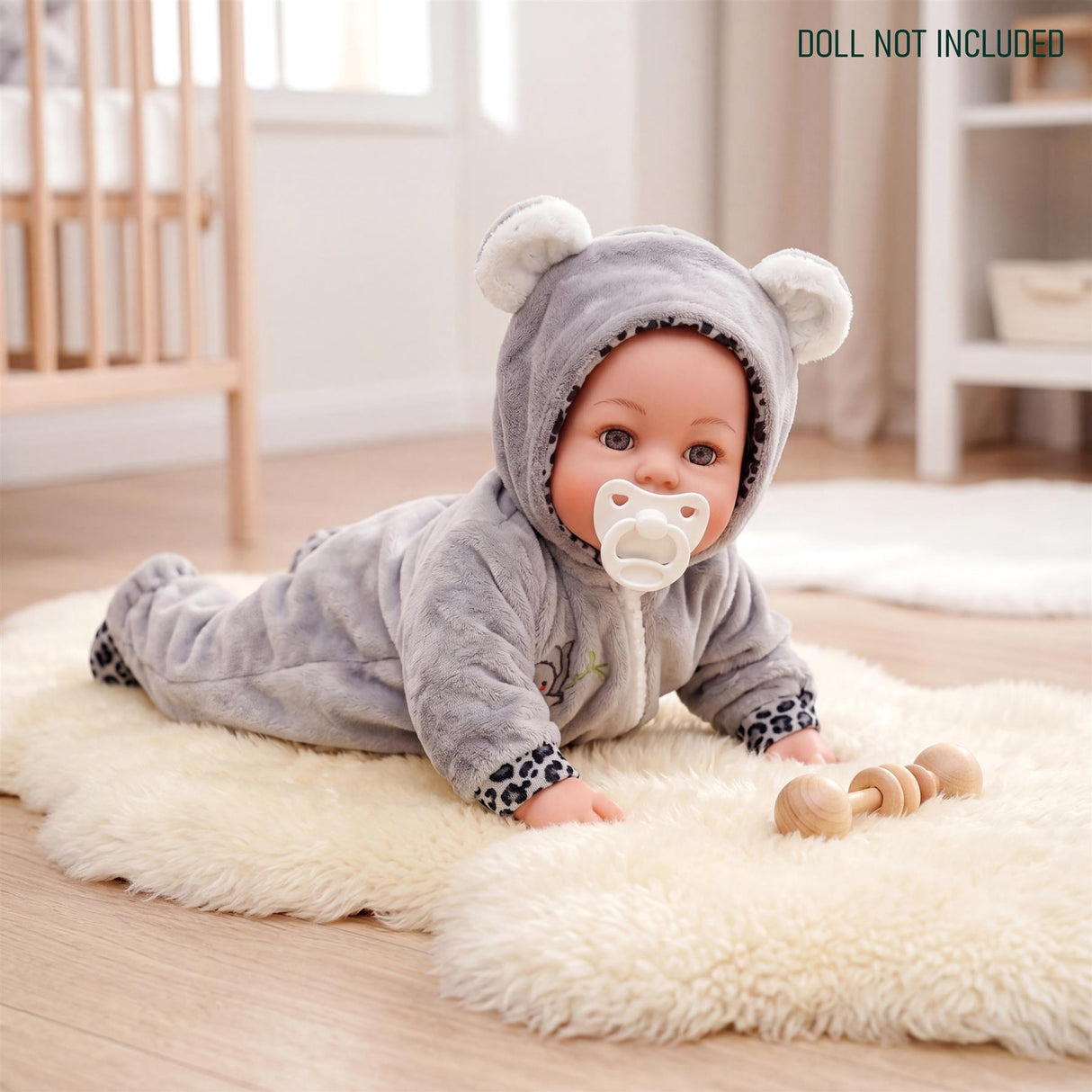 A doll wearing a gray hooded sleeper lies on a fluffy rug with wooden teething rings nearby.