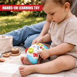 A baby wearing a beige top sits on a blanket outdoors, playing with a Game Controller Toy from The Magic Toy Shop