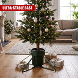 Green metal Christmas tree stand holding a decorated tree on wooden floor with presents nearby
