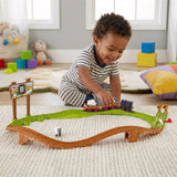 A young child plays with a train set containing tracks, engines, and accessories spread on the floor.