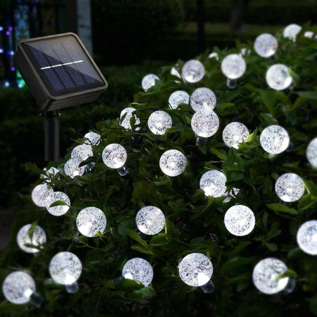 Solar panel powers circular lights woven into dense green shrubbery in a garden setting.