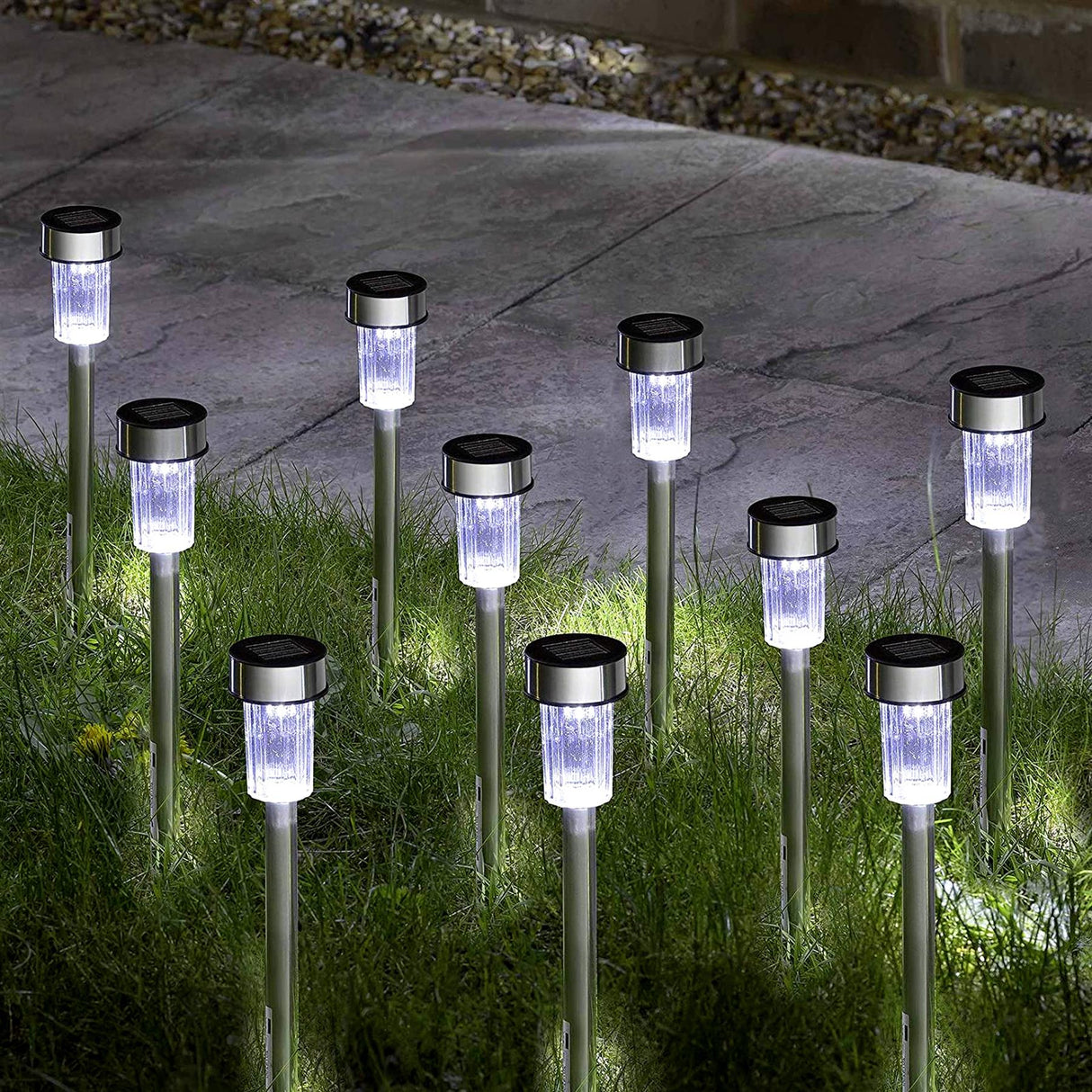 Row of illuminated, cylindrical solar stake lights placed among green garden grass.
