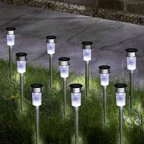 Row of illuminated, cylindrical solar stake lights placed among green garden grass.