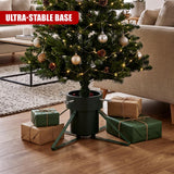 Metal medium Christmas tree stand by GEEZY holding a decorated tree and surrounded by gifts on a wooden floor