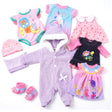 Six doll clothing pieces featuring jumpsuits, dresses, tops, and accessories in pink and lavender colors.