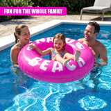 A pink inflatable ring spelling "BEACH" floats in a swimming pool surrounded by family members.