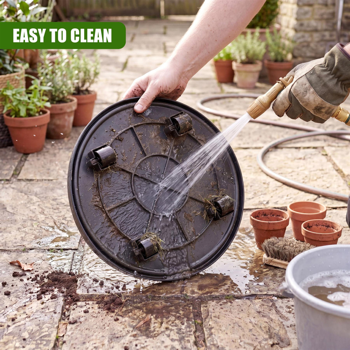 Hand sprays water on a dark, circular, wheeled caddy placed on outdoor stone patio tiles.
