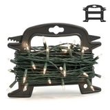 A black plastic Christmas light reel storage holder with a tangled green string of lit fairy lights coiled inside it