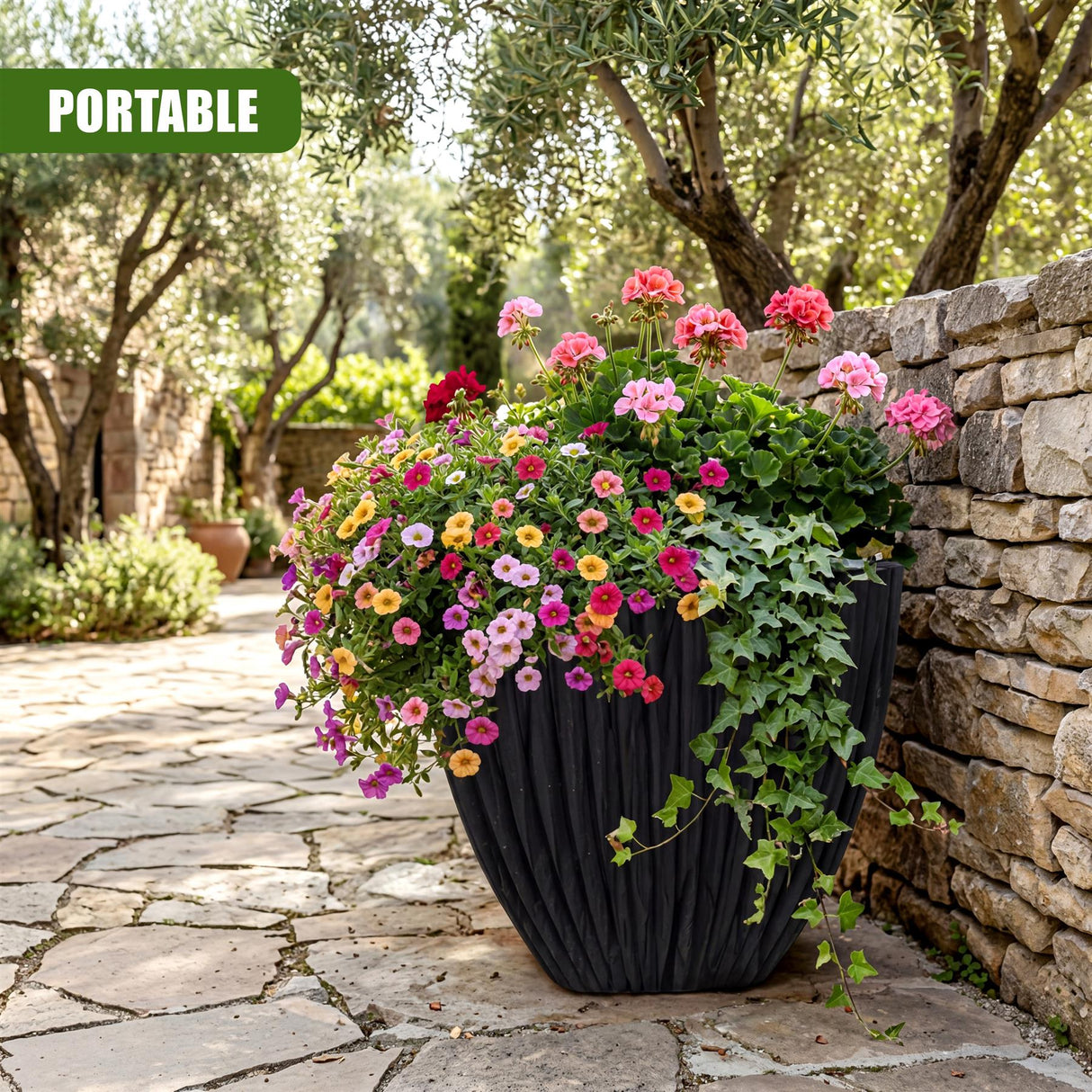 Large charcoal black planter holding vibrant mixed flowers and trailing green ivy on a stone patio.