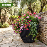 Large charcoal black planter holding vibrant mixed flowers and trailing green ivy on a stone patio.