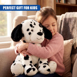 Child sitting on sofa embracing a black and white spotted Dalmatian plush toy.