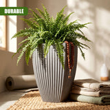 A tall, ribbed gray vase holds vibrant green fern plants and hanging wooden decorative beads.